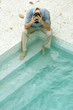 Man sitting with feet in pool, holding head, high angle view