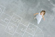 Photo: Little girl standing next to hopscotch squares, smiling up at camera, high angle view Little girl standing next to hopscotch squares, smiling up at camera, high angle view