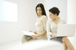 Photo: Two female professionals sitting together, discussing document, one holding laptop computer Two female professionals sitting together, discussing document, one holding laptop computer