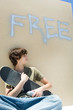 Teen boy holding skateboard and spray paint can, under the word free" on wall"