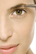 Woman tweezing eyebrow, looking at camera, cropped view