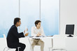 Businessmen sitting at table, looking at monitor, teleconferencing