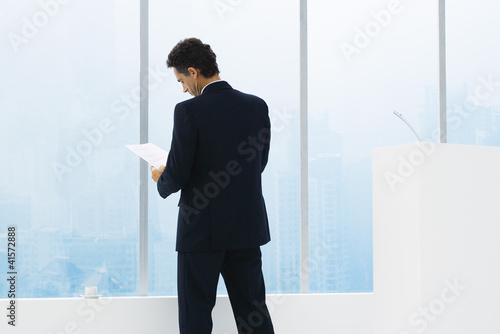 Photo: Businessman reviewing document, standing, rear view Businessman reviewing document, standing, rear view