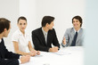 Business associates sitting around conference table, looking at each other, smiling