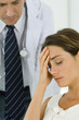 Woman holding head, doctor leaning behind her