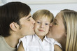 Parents kissing little boy's cheeks, boy looking at camera