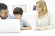 Father and son using laptop computer together, mother watching