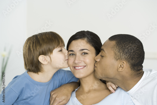 Photo: Husband and son kissing woman's cheeks, woman smiling at camera Husband and son kissing woman's cheeks, woman smiling at camera