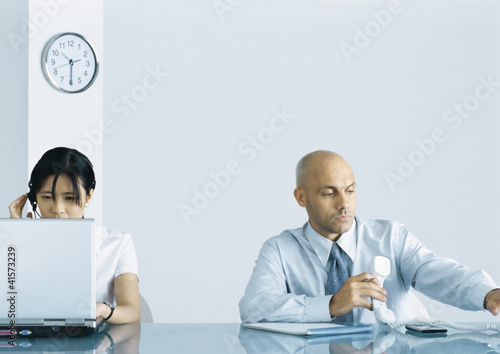 Photo: Office, man holding telephone while woman uses computer Office, man holding telephone while woman uses computer