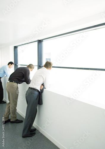 Photo: Three businessmen leaning on balcony in office building Three businessmen leaning on balcony in office building