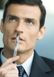 Businessman holding pen in front of mouth