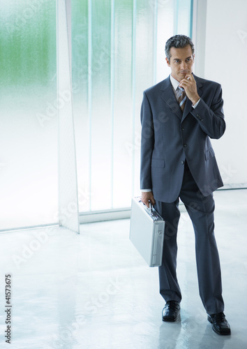 Photo: Businessman standing in lobby, holding briefcase Businessman standing in lobby, holding briefcase