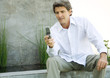 Man sitting in front of home, reading message on cell phone