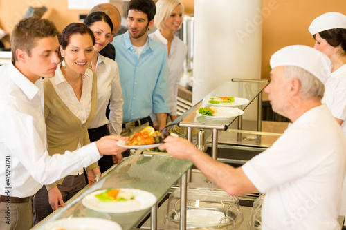 Photo: Office colleagues in canteen cook serve meals Office colleagues in canteen cook serve meals