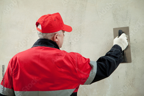 Photo: Plasterer in uniform working with float against the wall Plasterer in uniform working with float against the wall