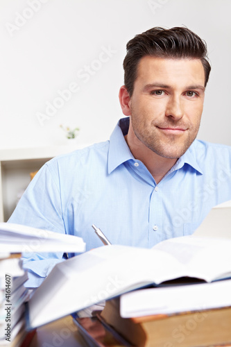 Foto: Mann lernt zwischen Bücherstapeln Mann lernt zwischen Bücherstapeln