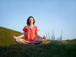 Foto: The young woman meditates on a green hill, in a lotus pose The young woman meditates on a green hill, in a lotus pose