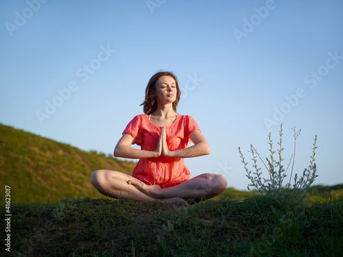 Foto: The young woman meditates on a green hill, in a lotus pose The young woman meditates on a green hill, in a lotus pose