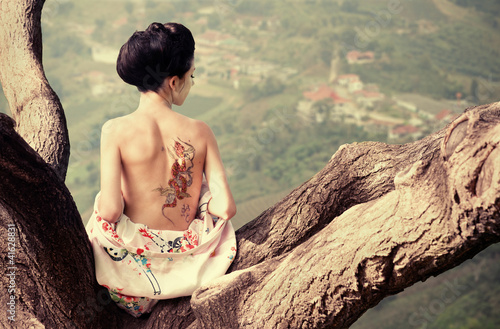 Photo: Woman with snake tattoo sitting on tree branch Woman with snake tattoo sitting on tree branch