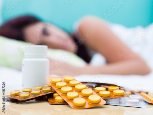 Photo: Sick woman in bed and pills from her medical treatment Sick woman in bed and pills from her medical treatment