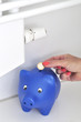 Frauenhand steckt 1 Euro in ein Sparschwein an einer Heizung