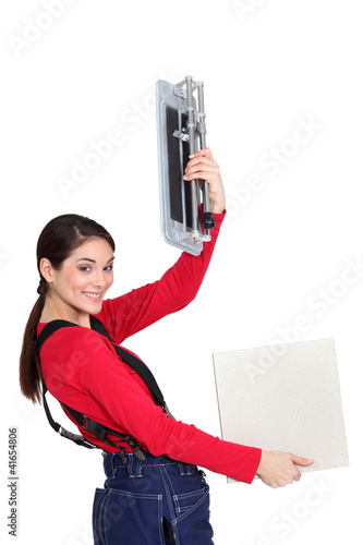 Photo: Tradeswoman holding up a tile cutting machine and a tile Tradeswoman holding up a tile cutting machine and a tile