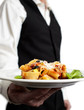 A waiter serves pasta. Focus on plate. Close-up.