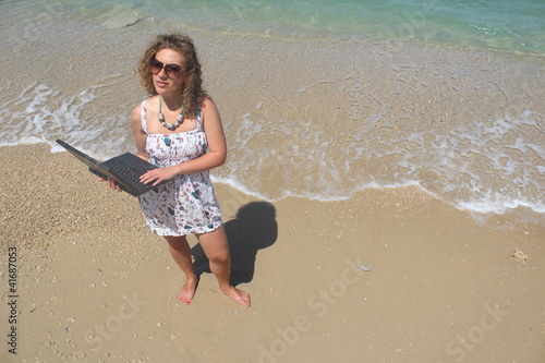 Photo: Curly hair young woman with her laptop at the beach Curly hair young woman with her laptop at the beach