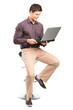 Young man sitiing on a stool and working on a laptop Young man sitiing on a stool and working on a laptop
