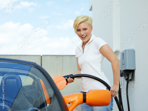 Photo: Pretty woman is loading electrically powered car outdoors Pretty woman is loading electrically powered car outdoors