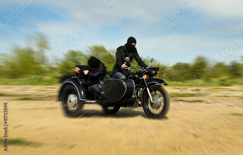 Photo: Two armed men riding a motorcycle with a sidecar. Motion blur. Two armed men riding a motorcycle with a sidecar. Motion blur.