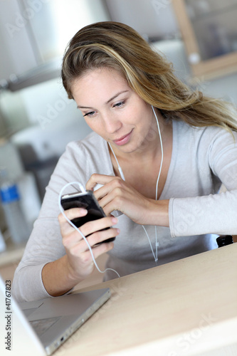 Photo: Young woman using smartphone at home with earphones Young woman using smartphone at home with earphones