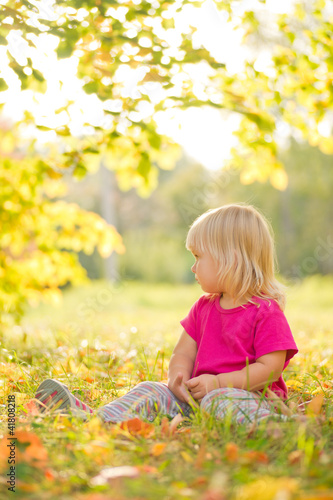 Photo: Adorable baby sit on grass with leaf under trees shadow on sunse Adorable baby sit on grass with leaf under trees shadow on sunse