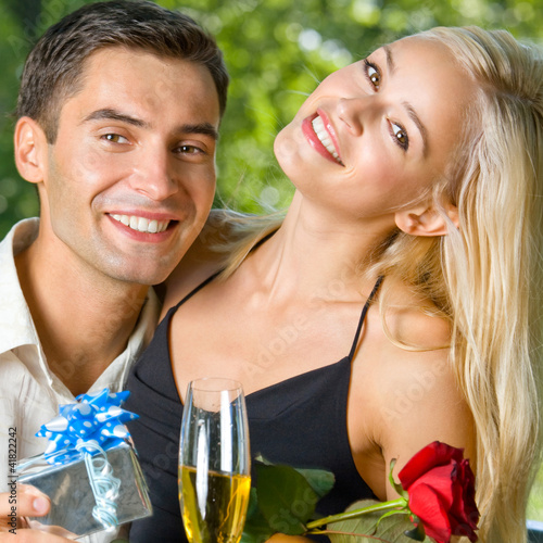 Foto: Young couple with gifts, rosa and champagne, outdoor Young couple with gifts, rosa and champagne, outdoor
