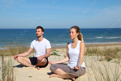 Photo: Couple doing yoga exercices on a sandy beach Couple doing yoga exercices on a sandy beach