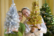 Photo: Couple by Christmas tree with small ornamental trees, smiling, portrait Couple by Christmas tree with small ornamental trees, smiling, portrait