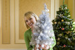 Photo: Woman by Christmas tree with small ornamental tree, smiling, portrait Woman by Christmas tree with small ornamental tree, smiling, portrait