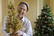 Photo: Mature man by Christmas tree with small ornamental tree, smiling, portrait Mature man by Christmas tree with small ornamental tree, smiling, portrait
