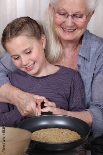 Photo: Girl and her granny cooking pancakes Girl and her granny cooking pancakes