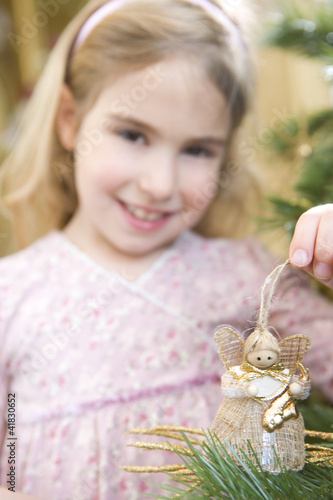 Foto: Girl (4-6) with angel decoration by Christmas tree, smiling, portrait, close-up Girl (4-6) with angel decoration by Christmas tree, smiling, portrait, close-up