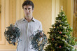 Photo: Young man with tangled bunches of Christmas lights by Christmas tree, portrait Young man with tangled bunches of Christmas lights by Christmas tree, portrait