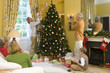 Foto: Family by Christmas tree, grandfather taking photograph of girl (5-7) putting angel decoration on tree Family by Christmas tree, grandfather taking photograph of girl (5-7) putting angel decoration on tree