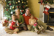 Family of four by Christmas tree with gifts, portrait