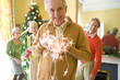 Photo: Senior man with Christmas lights, family and Christmas tree in background, portrait Senior man with Christmas lights, family and Christmas tree in background, portrait