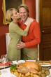 Woman kissing husband on cheek by turkey on dinner table, portrait of man