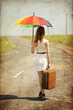 Lonely girl with suitcase and umrella at country road.