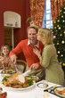Family having Christmas dinner, woman kissing husband cutting turkey