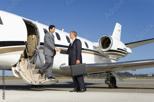 Photo: Businessman boarding aeroplane on runway, shaking hands with colleague Businessman boarding aeroplane on runway, shaking hands with colleague