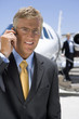 Photo: Businessman in glasses with hand on earpiece by aeroplane on runway, smiling, portrait Businessman in glasses with hand on earpiece by aeroplane on runway, smiling, portrait