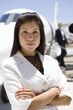 Businesswoman with arms crossed by aeroplane on runway, portrait
